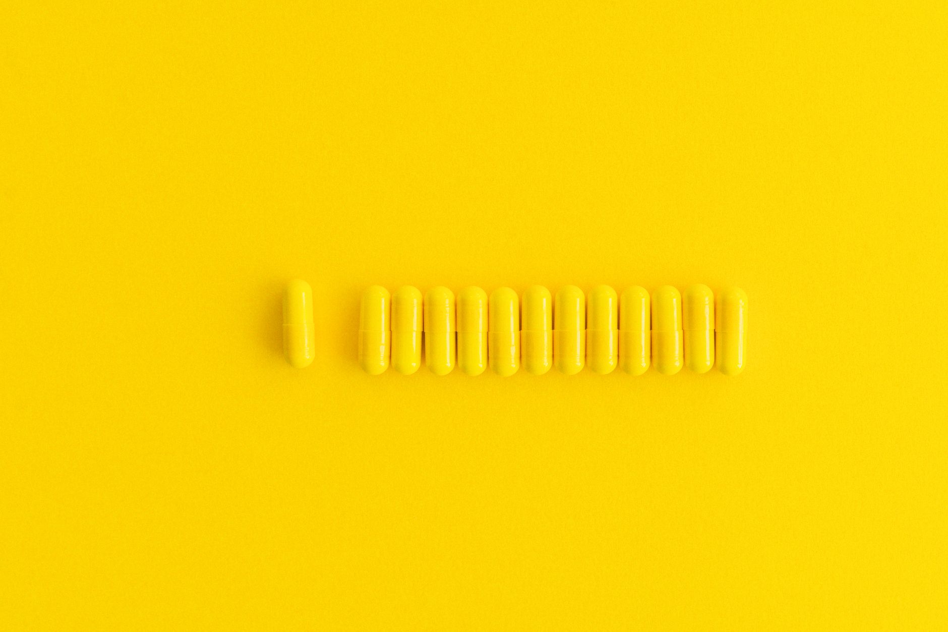 Close-up of yellow capsules lined up on a vibrant yellow background, perfect for healthcare themes.